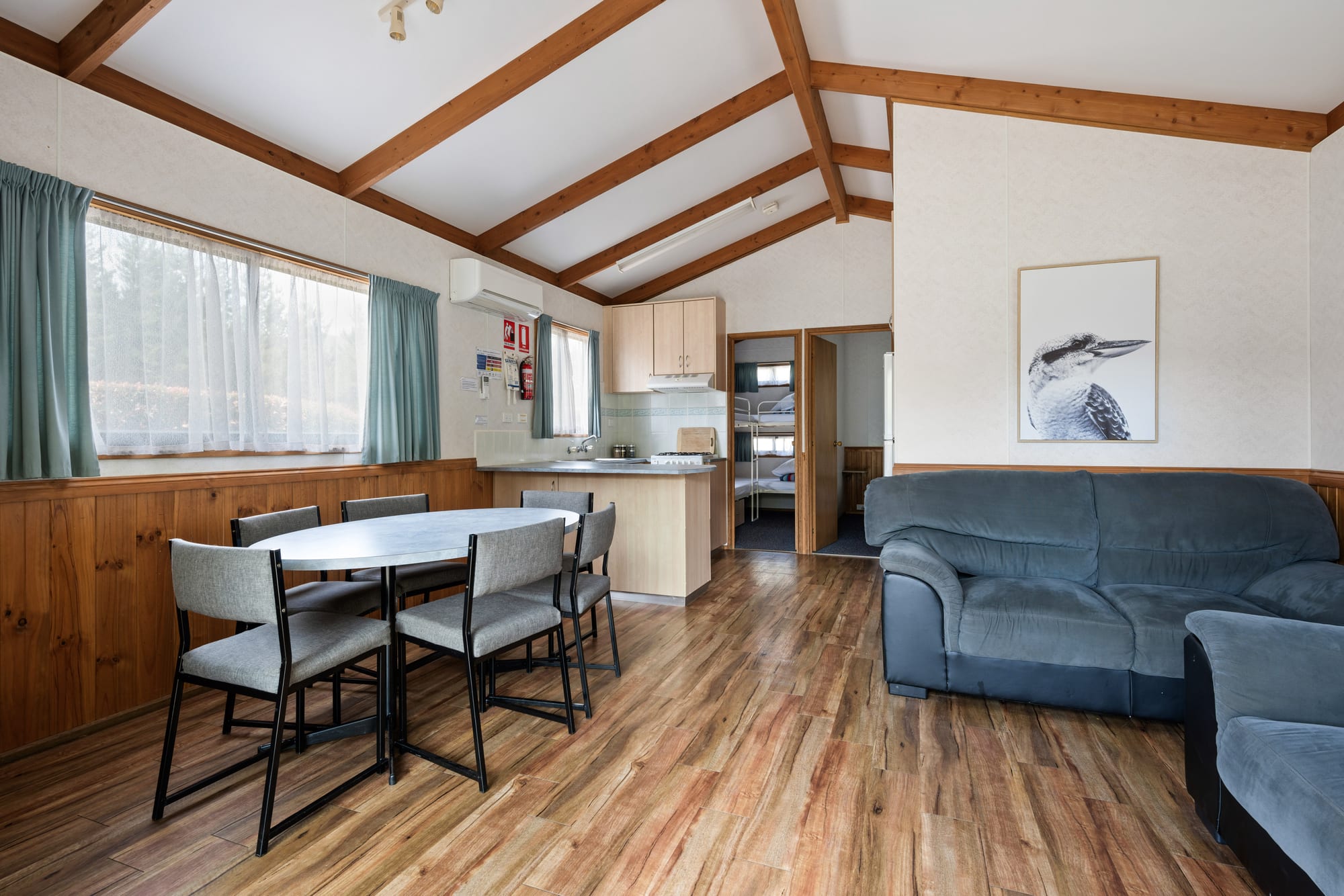 Open-plan family cabin interior at Bright Accommodation Park with dining area, kitchenette, lounge, and exposed timber beams