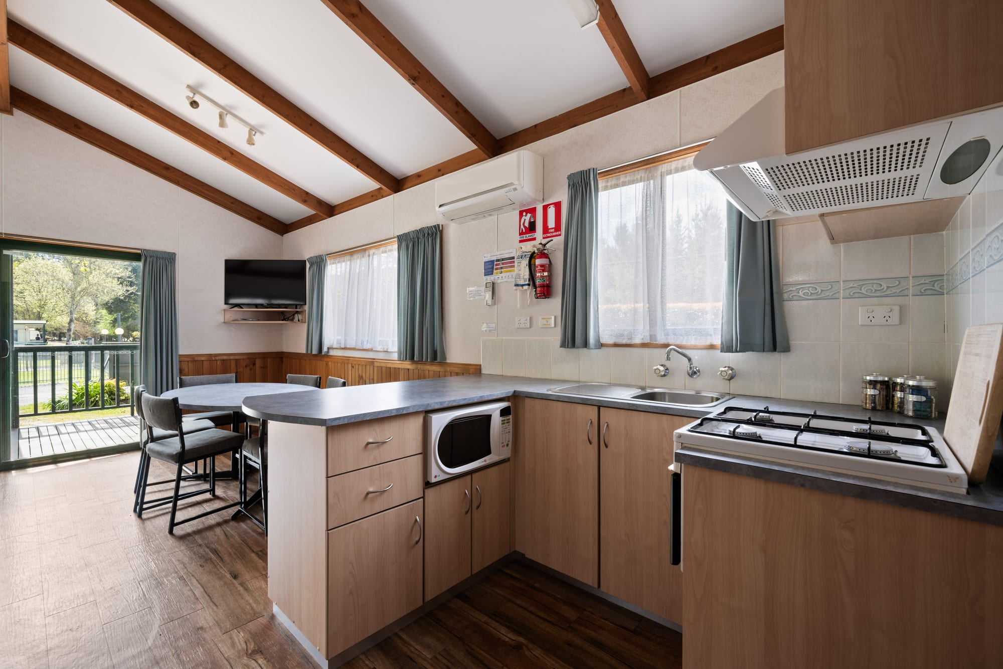 Family cabin kitchen and dining area at Bright Accommodation Park with gas cooktop, microwave and deck access