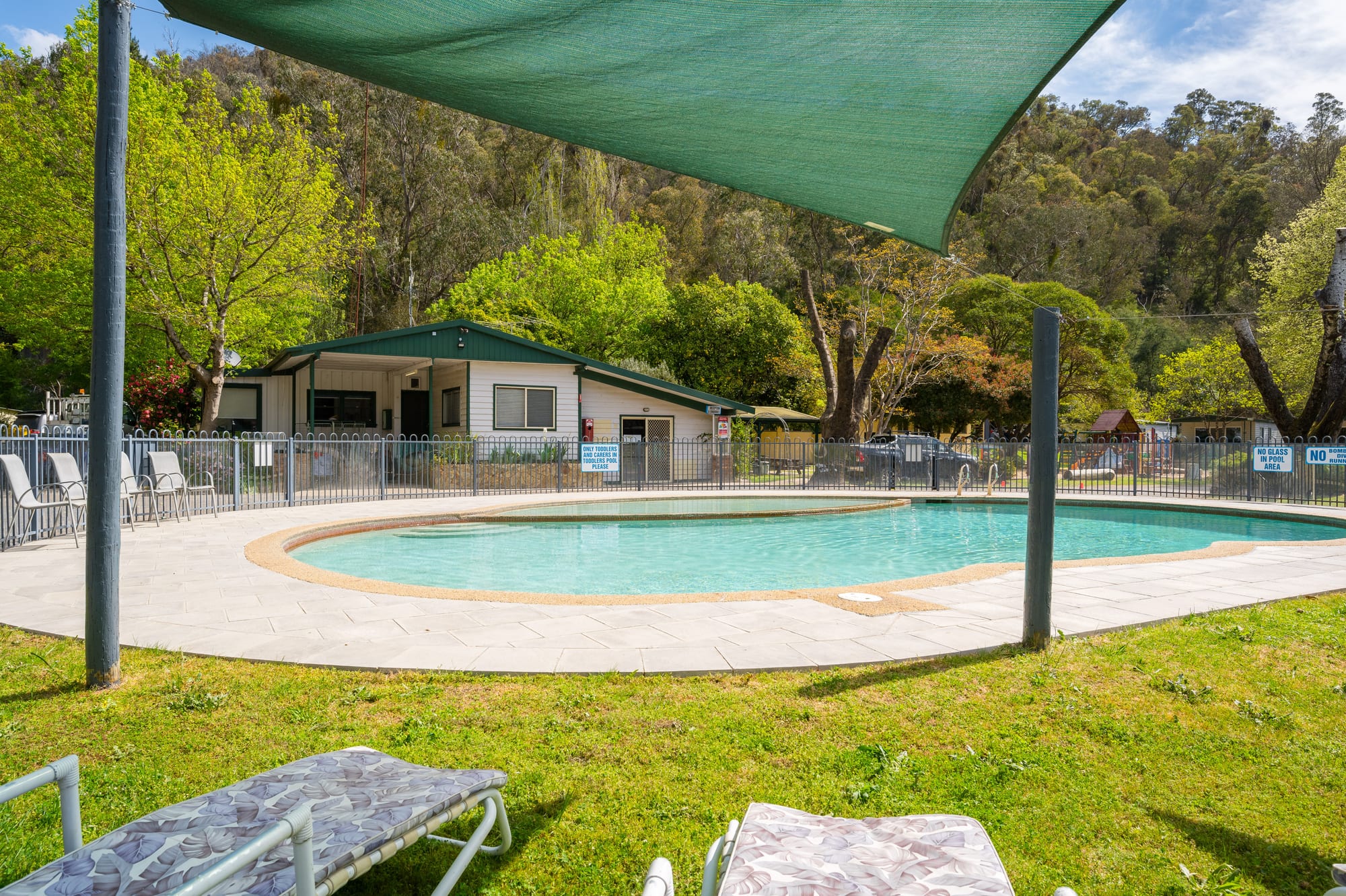 Outdoor swimming pool with shade sails at Bright Accommodation Park, surrounded by native trees and mountain views