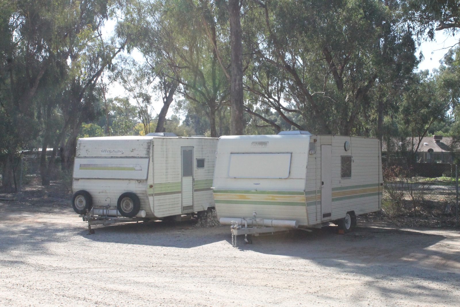 Two older caravans parked on a gravel storage area under gum trees at Torrumbarry Weir Holiday Park, Patho VIC