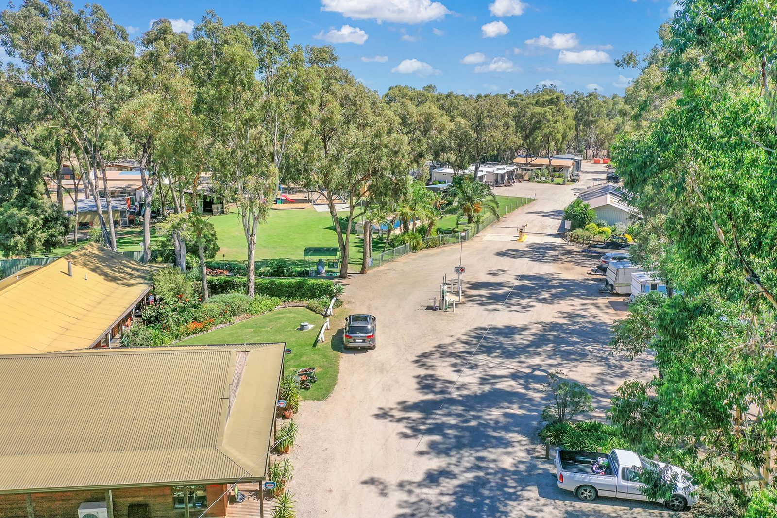 Low aerial along park road with cabins caravans and gum trees at Torrumbarry Weir Holiday Park