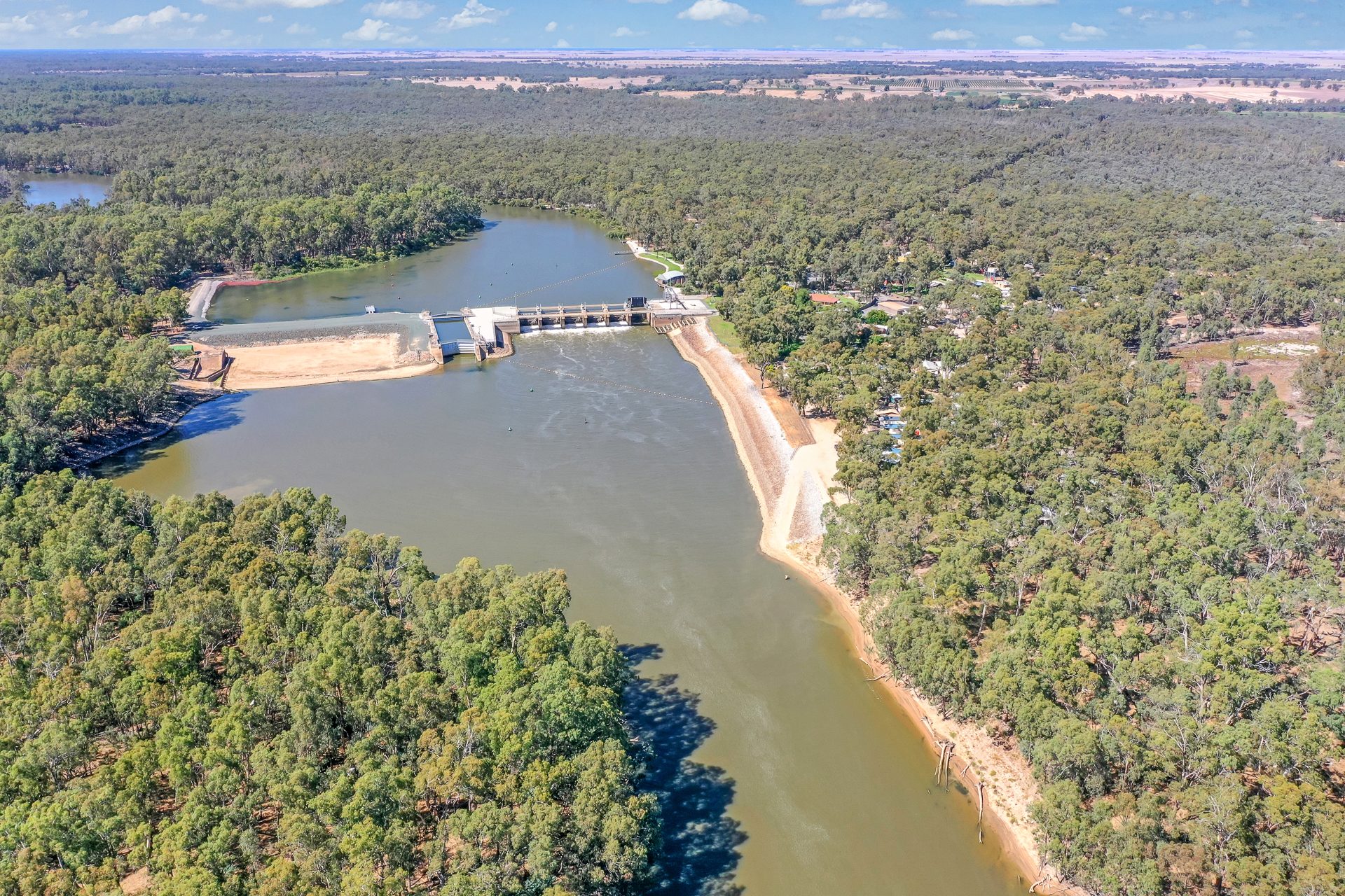 Aerial view of Torrumbarry Weir wall across the river, with the sandy river beach and gum tree bushland near Torrumbarry Weir Holiday Park
