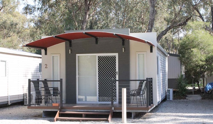 Cabin 2 at Torrumbarry Weir Holiday Park with curved red awning, timber deck and outdoor chairs under gum trees