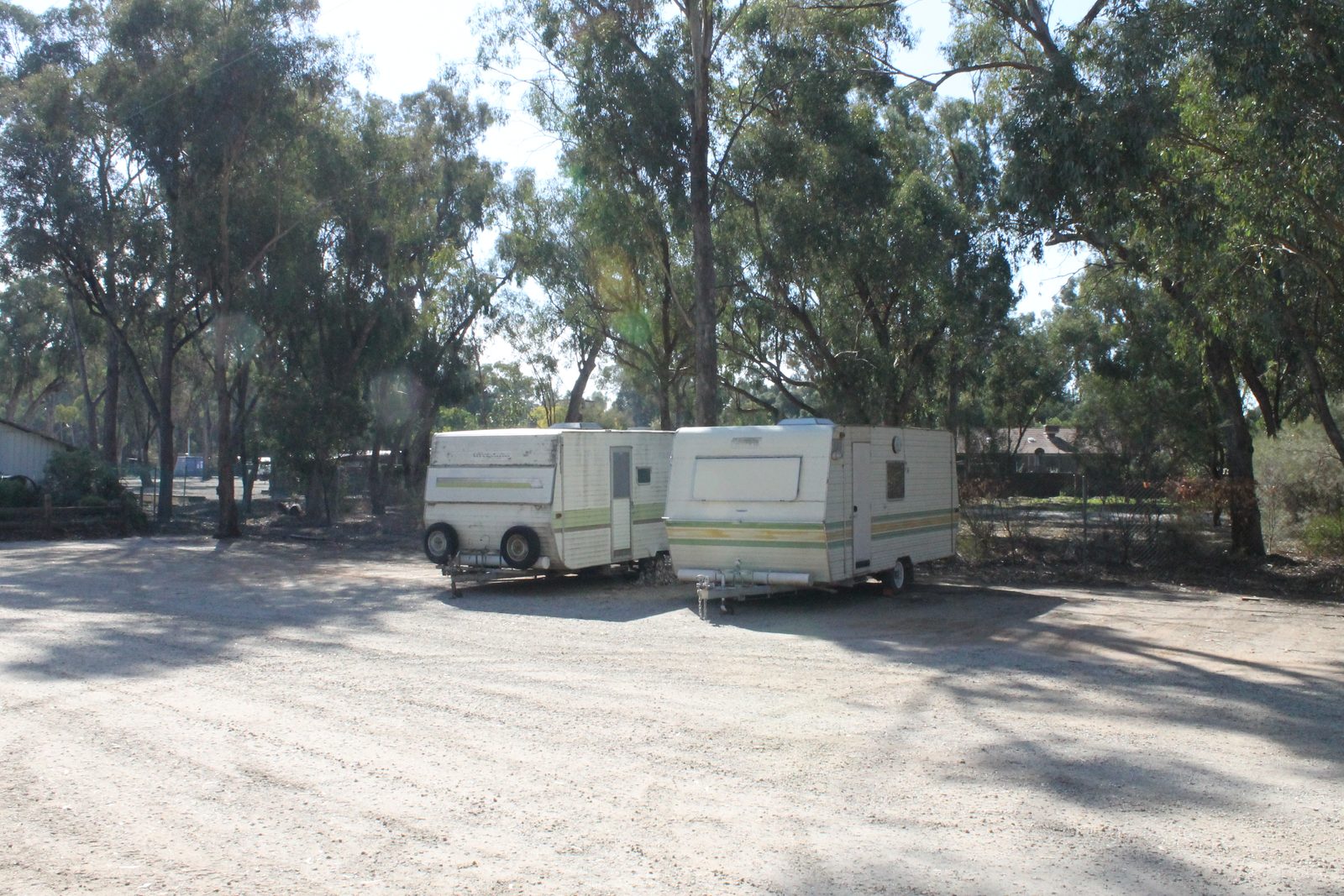 Two caravans parked on a gravel site shaded by tall gum trees at Torrumbarry Weir Holiday Park, Patho VIC