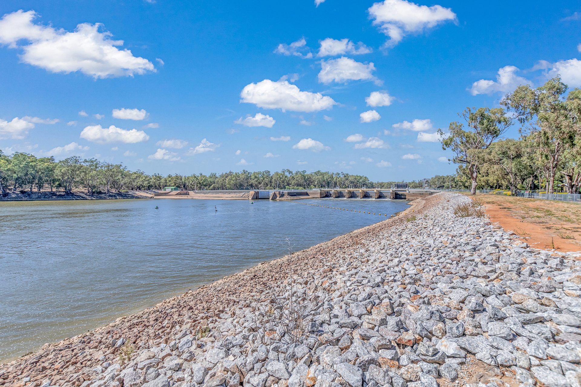 Murray river with weir wall in the distance rocky bank foreground at Torrumbarry Weir Holiday Park