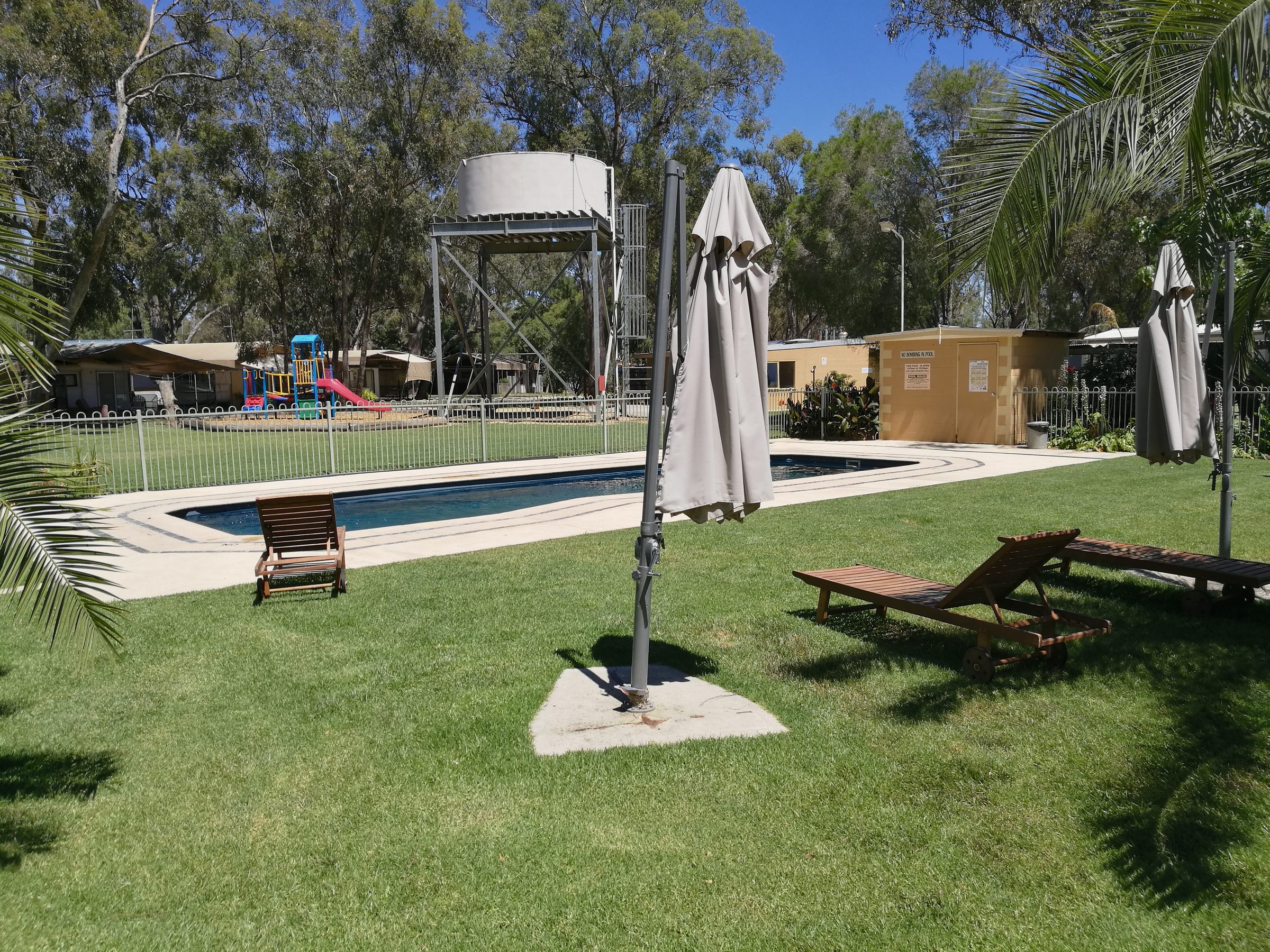 Swimming pool with timber sun loungers and closed umbrellas on lawn at Torrumbarry Weir Holiday Park