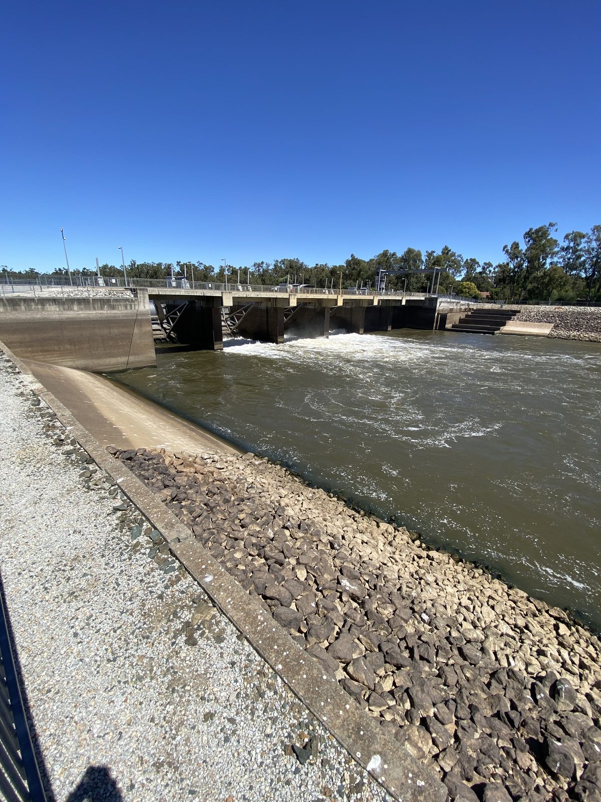 Weir gates and outflow channel seen along the stone bank at Torrumbarry Weir Holiday Park