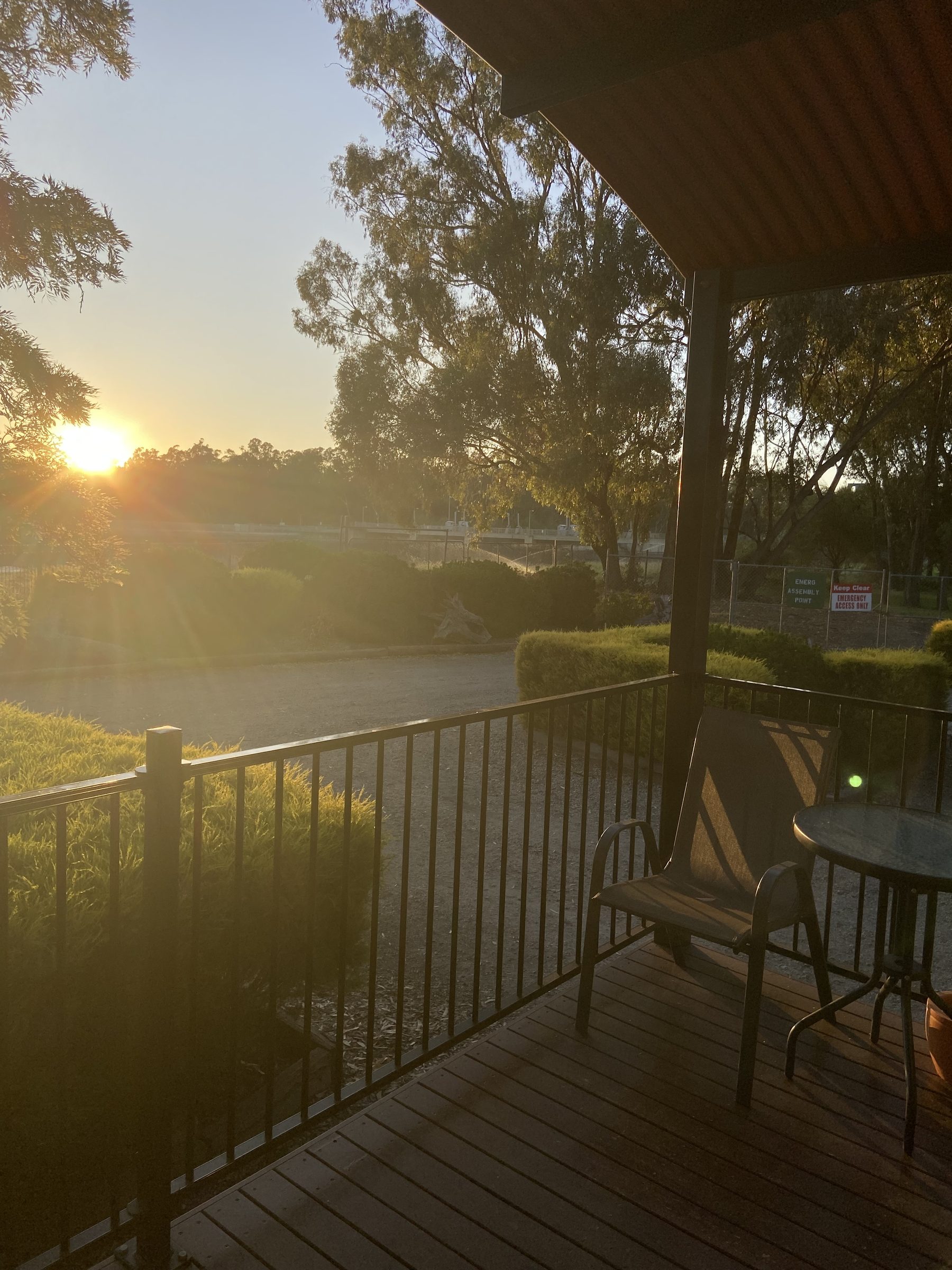 Covered cabin deck with outdoor table and chairs overlooking the weir at Torrumbarry Weir Holiday Park at sunrise