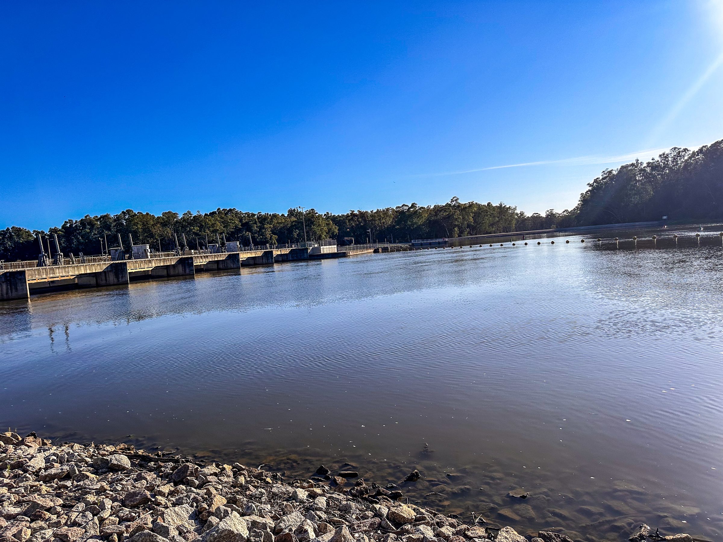 Calm murray river and rocky bank looking towards the weir at Torrumbarry Weir Holiday Park