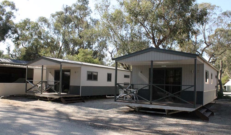 Two self-contained cabins with covered verandahs at Torrumbarry Weir Holiday Park, set among gum trees in Patho VIC