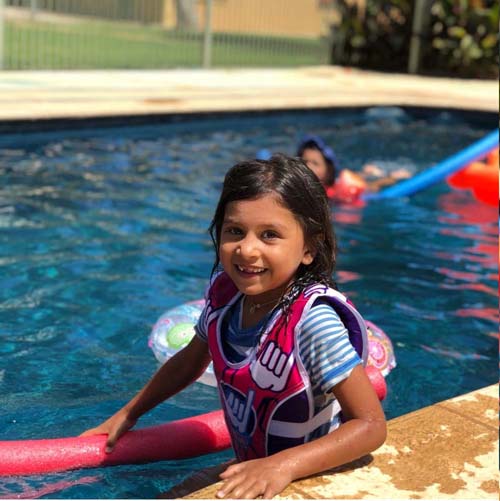 Young girl in a life vest smiling in the swimming pool at Torrumbarry Weir Holiday Park, Patho VIC, with a pool noodle