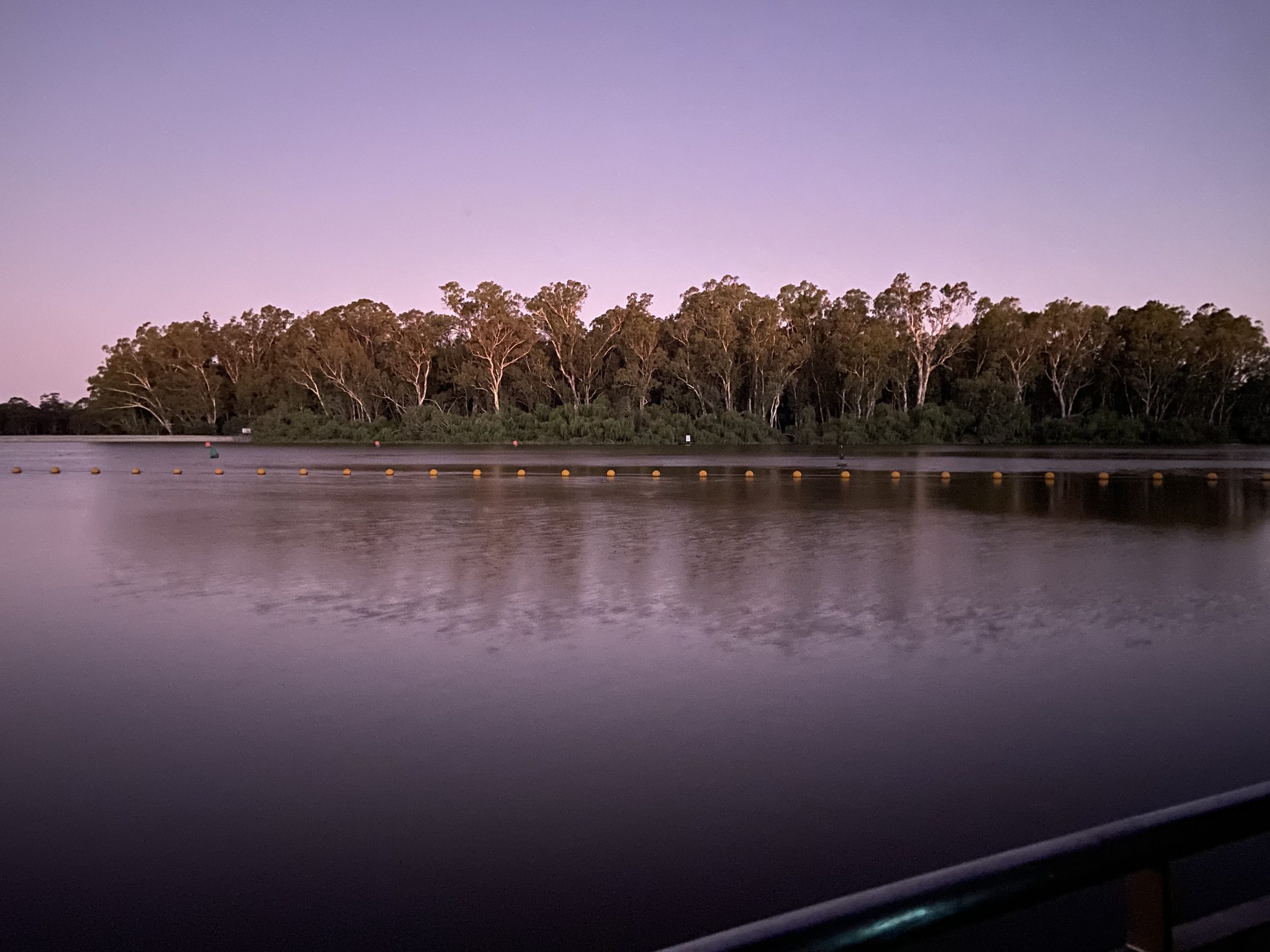 Glassy murray river at dusk reflecting a dark red gum treeline at Torrumbarry Weir Holiday Park