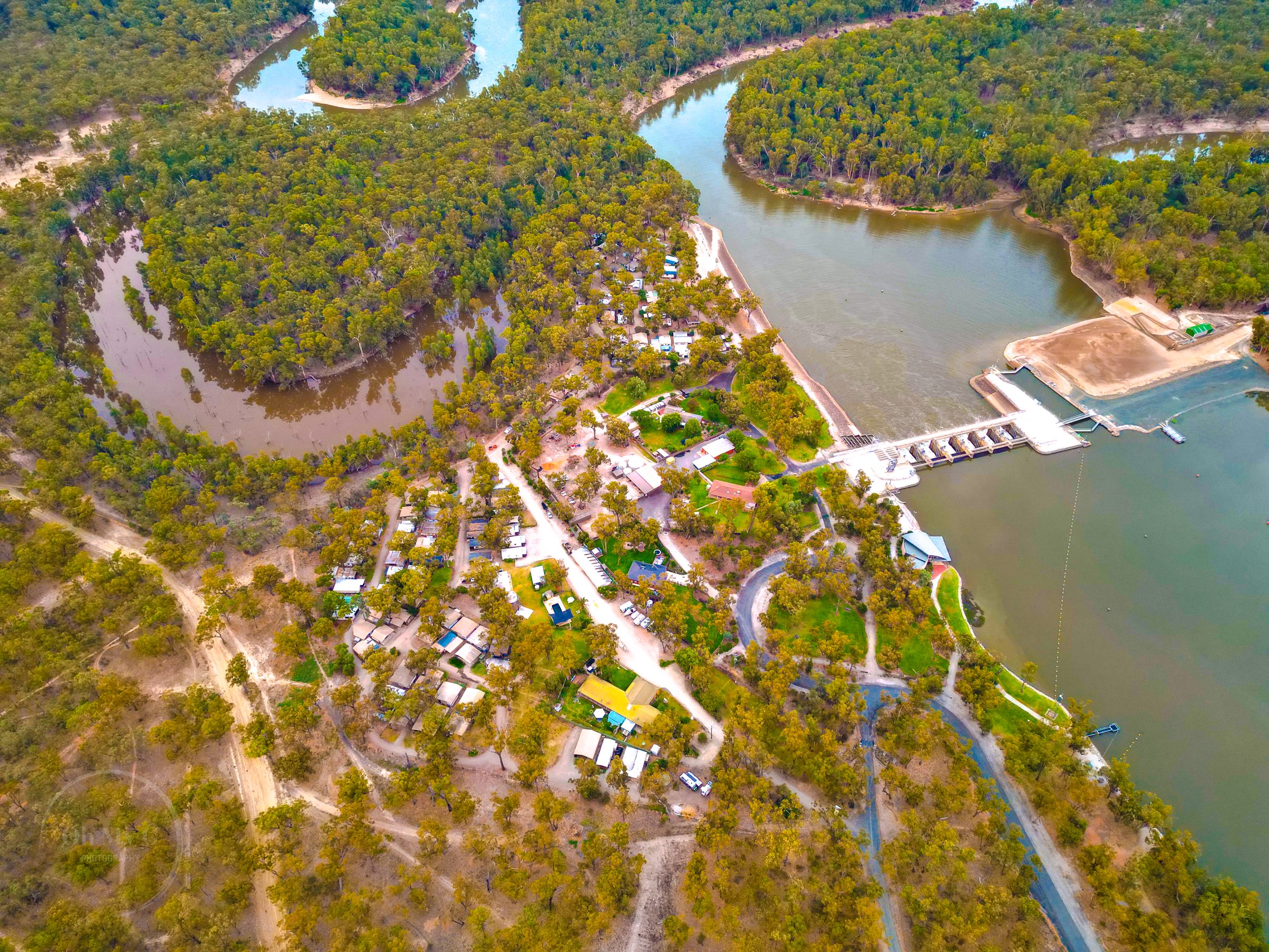Aerial of riverside park with weir and forest beyond at Torrumbarry Weir Holiday Park