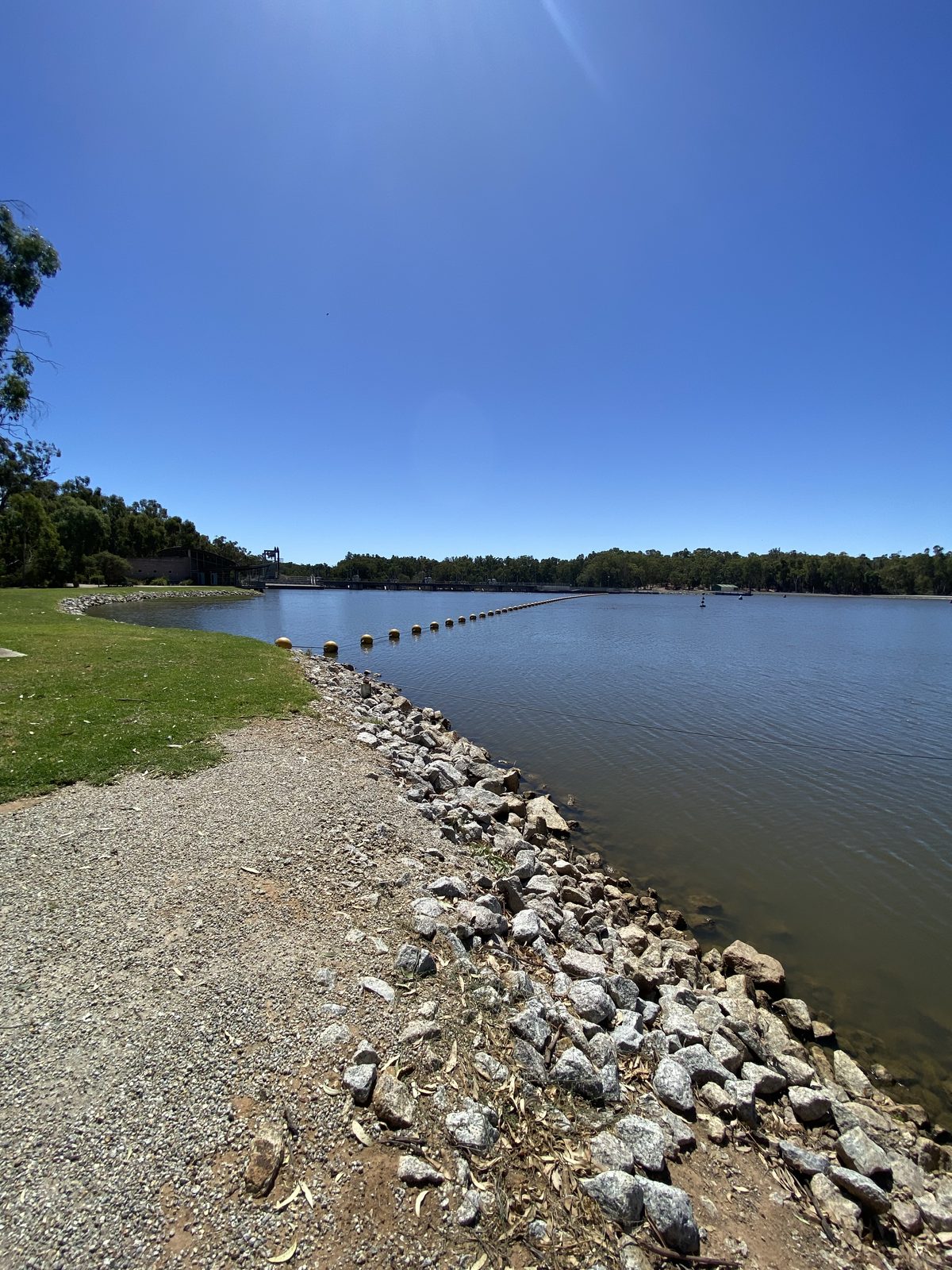 Stone-lined river bank curving away beside mown grass at Torrumbarry Weir Holiday Park