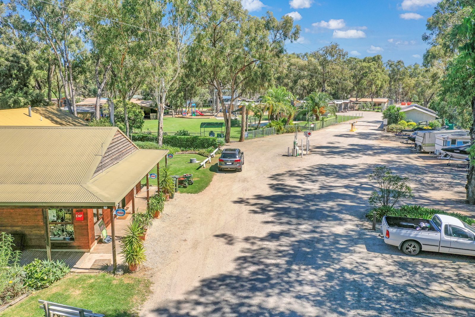 Low aerial over park entrance road cabin roofs and parked cars at Torrumbarry Weir Holiday Park