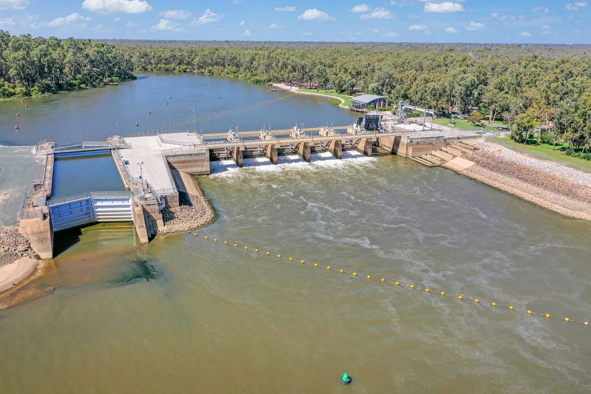 Aerial of weir gates with water flowing over the wall at Torrumbarry Weir Holiday Park