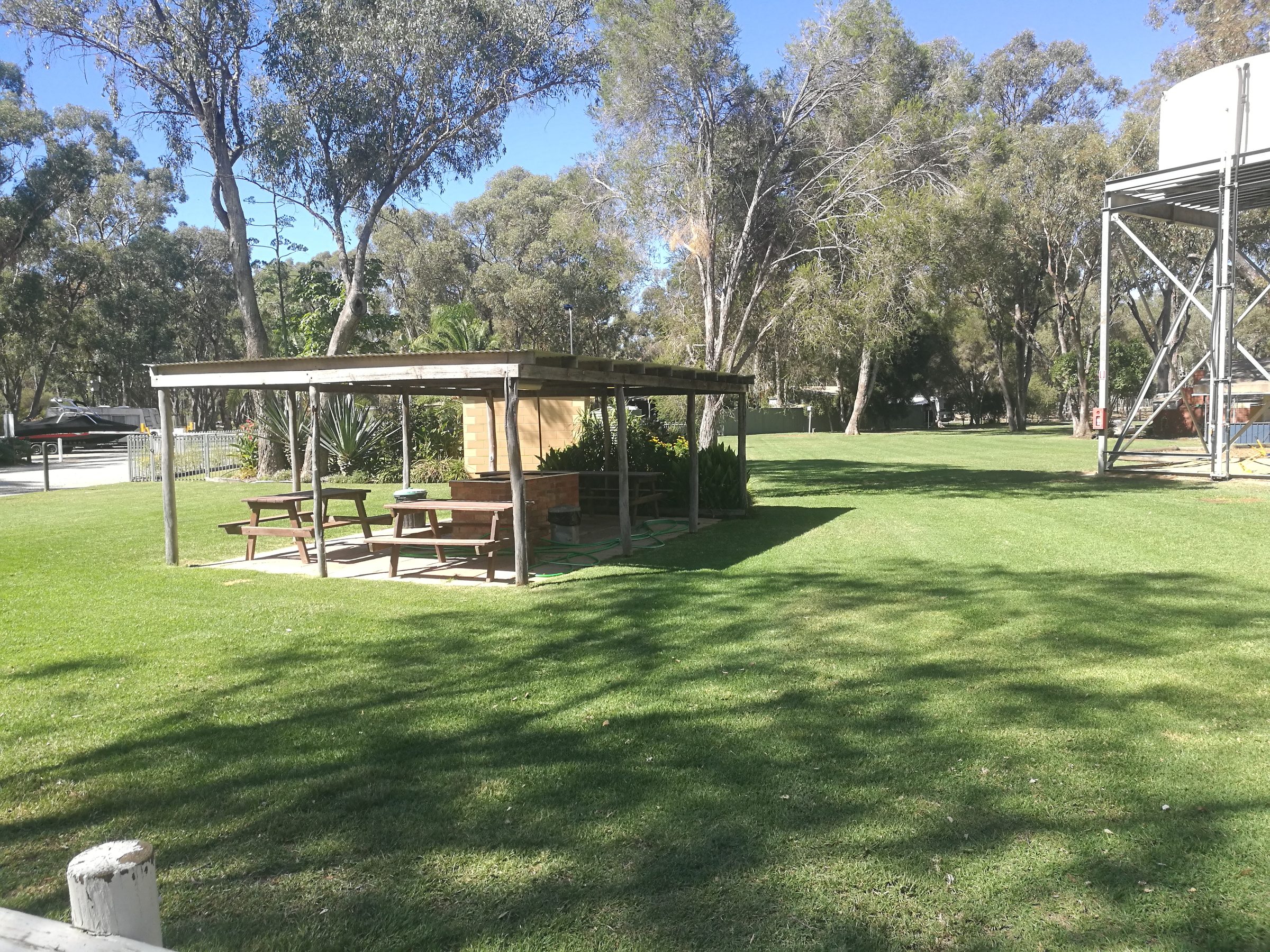 Open-sided timber camp kitchen shelter with brick BBQ and picnic tables on a shaded lawn at Torrumbarry Weir Holiday Park