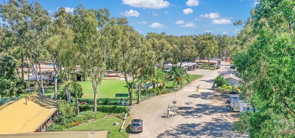 Aerial view of Torrumbarry Weir Holiday Park in Patho VIC, showing the gravel access road winding past cabins, caravans and towering gum trees