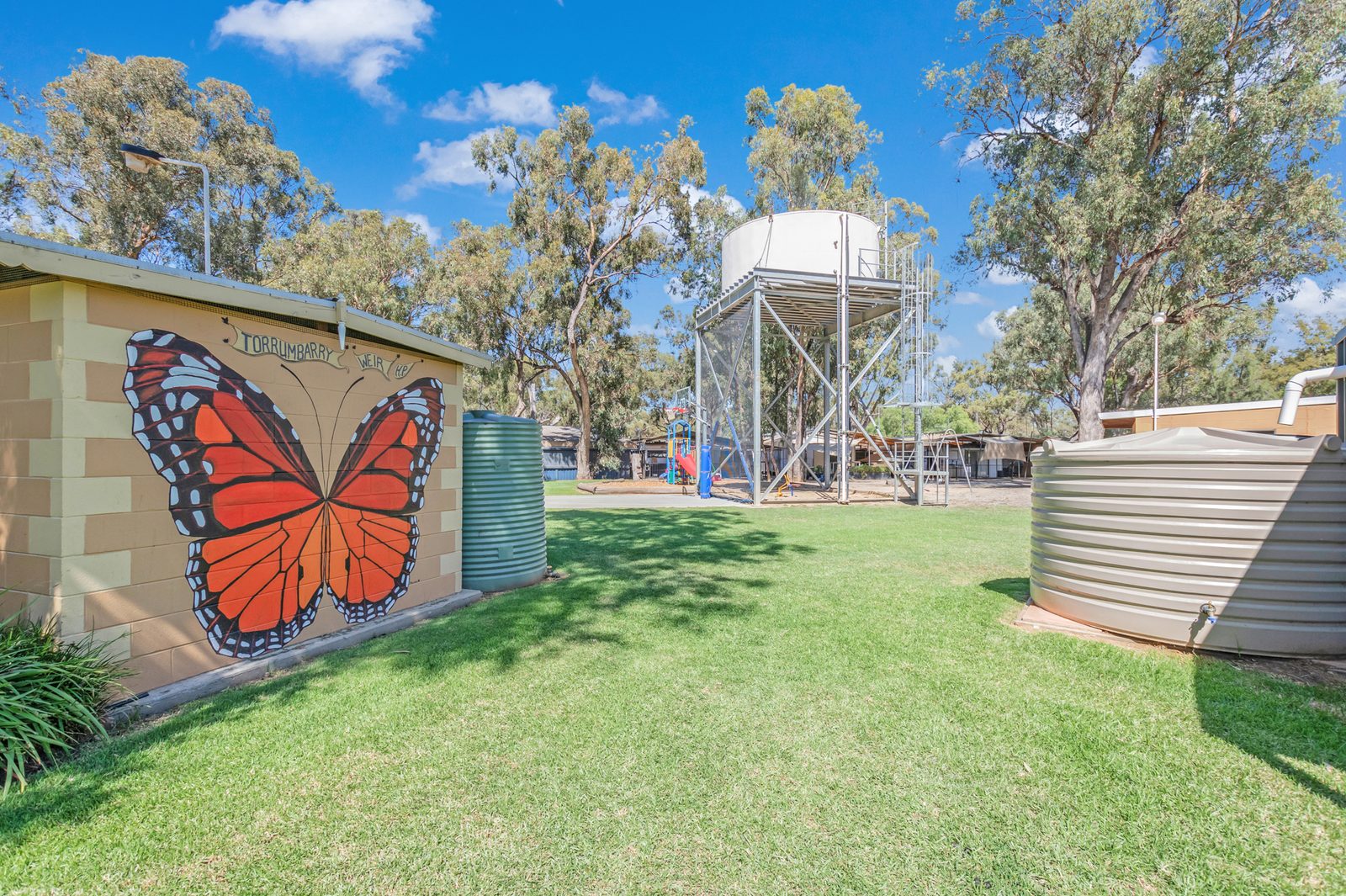 Orange monarch butterfly mural on the amenities block wall at Torrumbarry Weir Holiday Park, with green lawn and gum trees