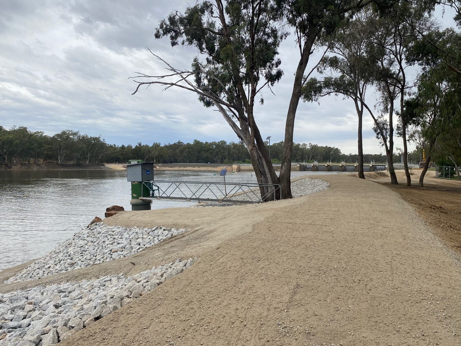 Gravel boat ramp track with rock walls beside the river at Torrumbarry Weir Holiday Park, weir structure visible upstream