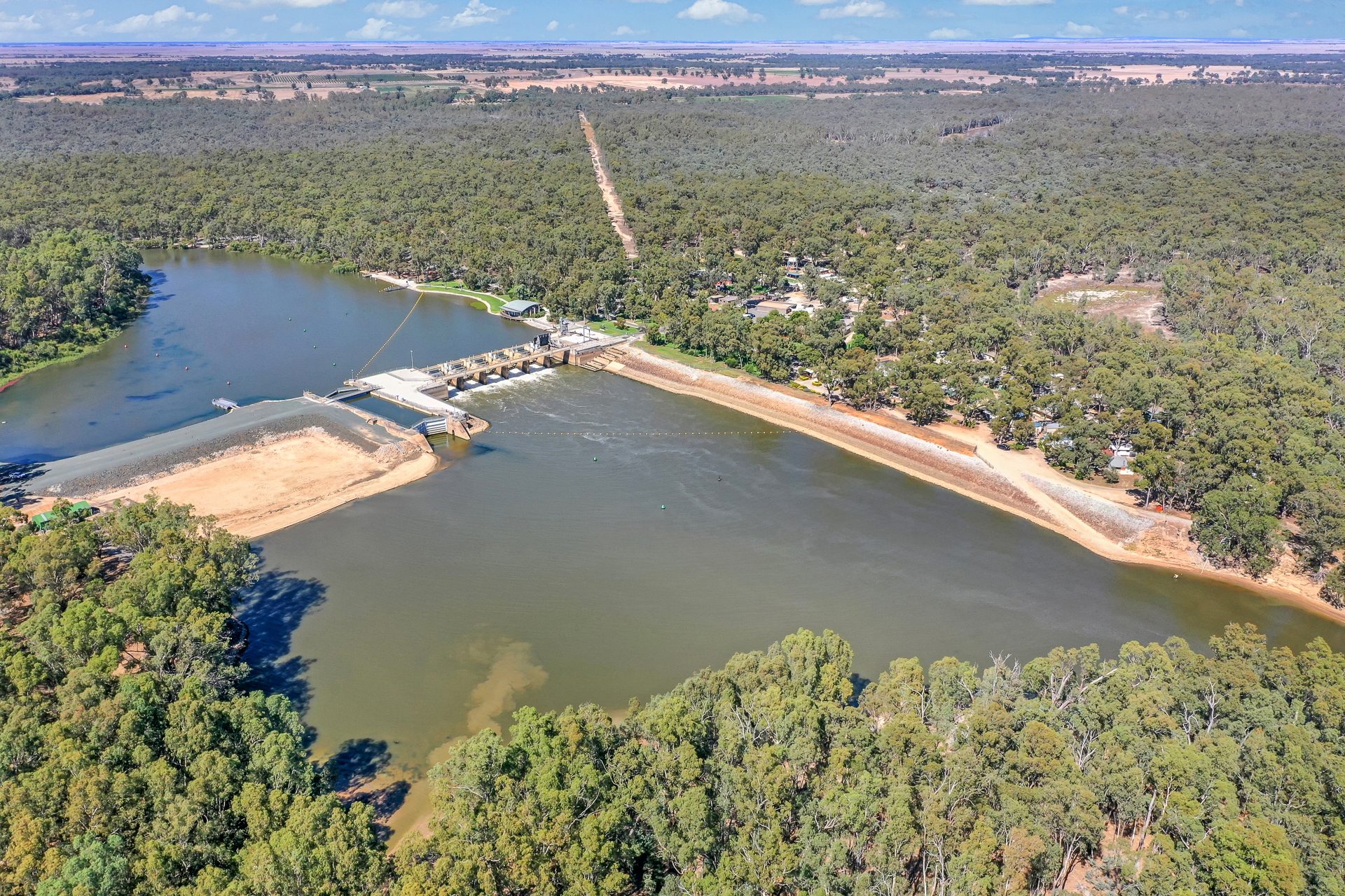 Aerial drone view of Torrumbarry Weir wall across the river channel, gum trees lining the banks near the holiday park at Patho VIC
