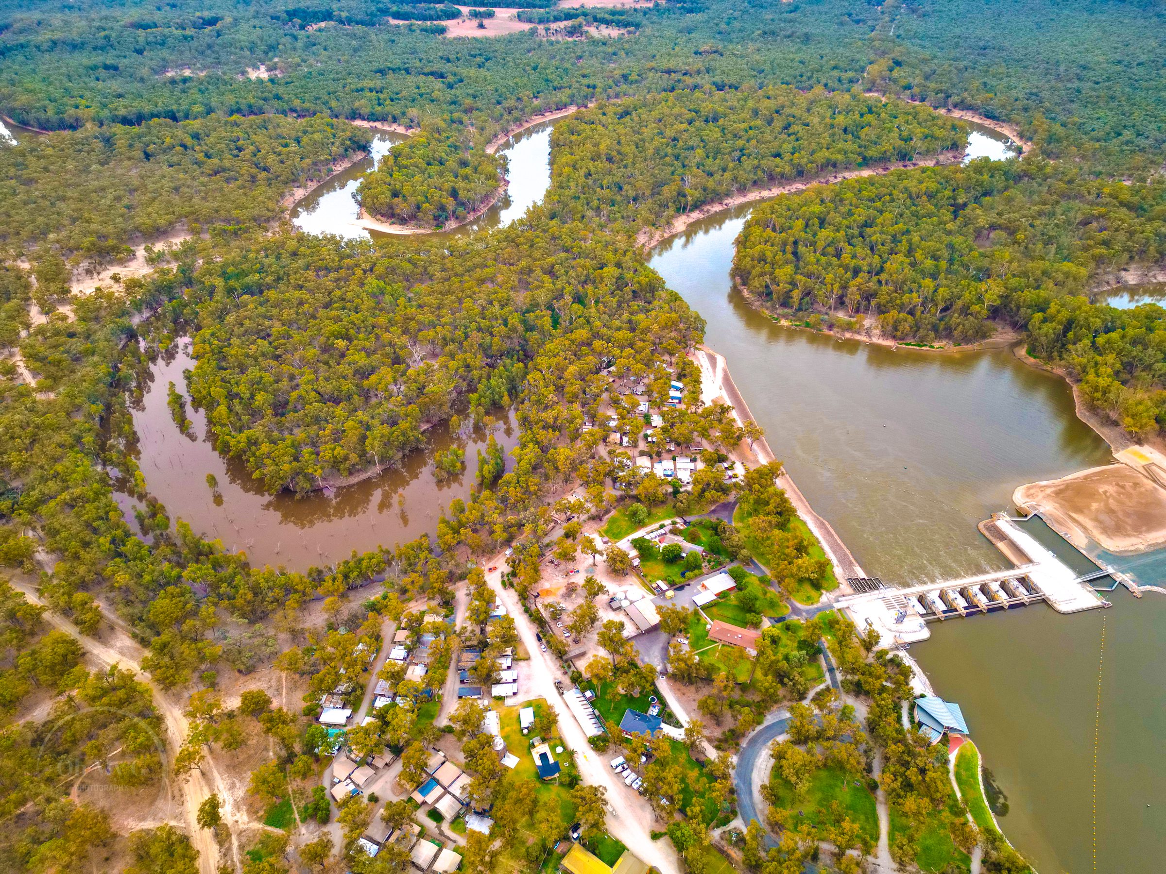 Aerial of river bend park grounds and weir in forest at Torrumbarry Weir Holiday Park