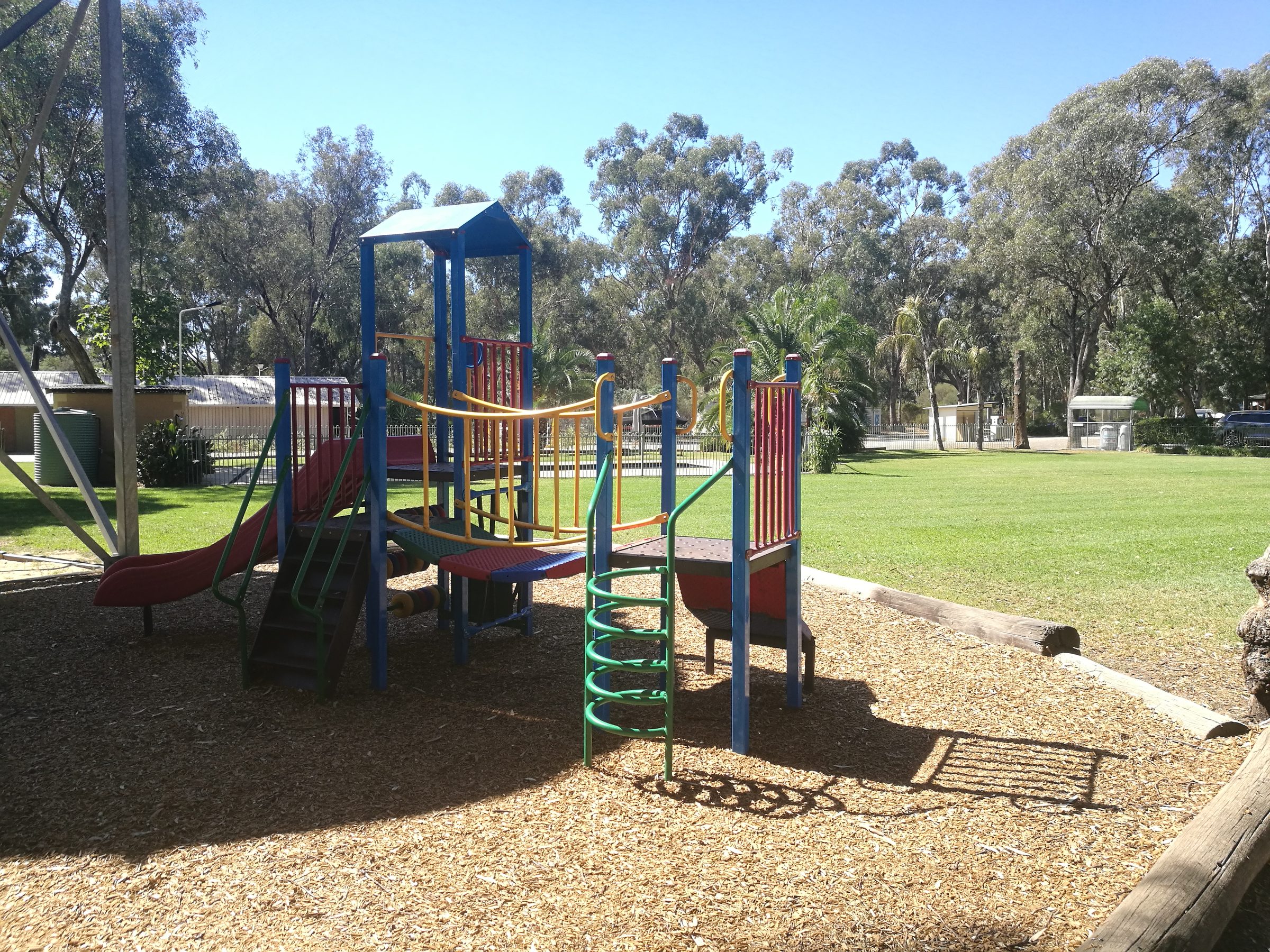 Colourful playground climbing frame with red slide and green spiral rope net at Torrumbarry Weir Holiday Park, Patho VIC