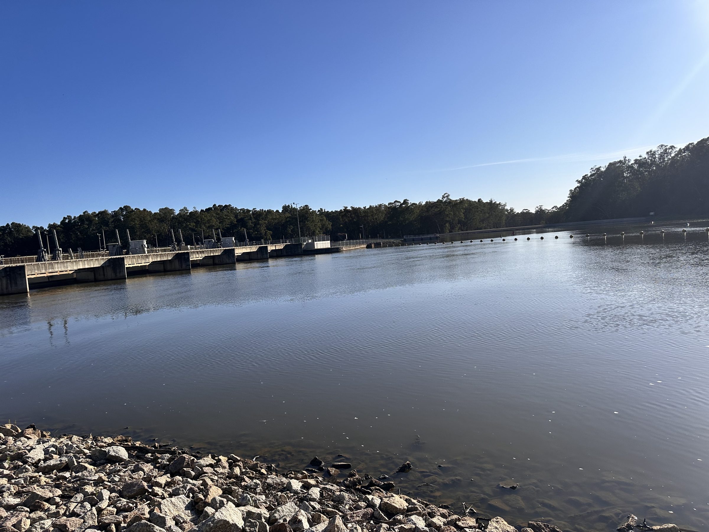 Calm murray river and rocky bank looking towards the weir at Torrumbarry Weir Holiday Park