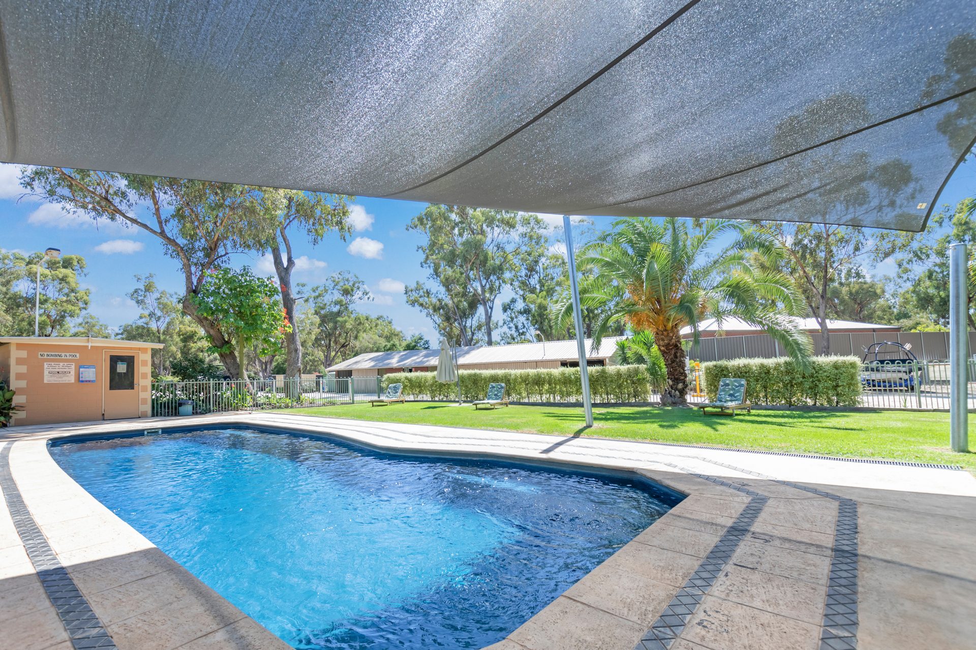 Sparkling swimming pool with shade sail and paved surround at Torrumbarry Weir Holiday Park caravan park, Patho VIC